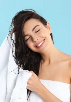 Young woman drying hair with towel on light blue background